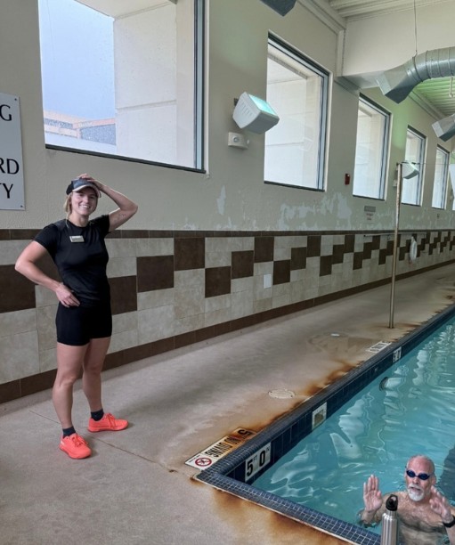 Christina coaching poolside while a swimmer waves from the lane